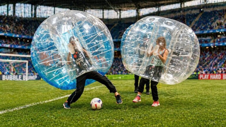 Deux joueurs en bulles transparentes en train de jouer au bubble foot sur un terrain en herbe avec public en arriere-plan