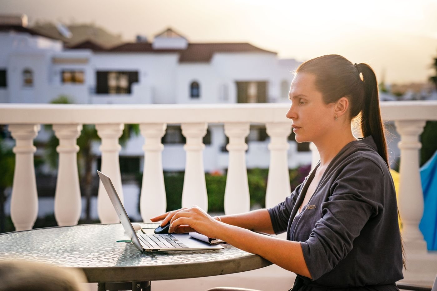 Salariée en télétravail à l'étranger, ordinateur portable sur un balcon ensoleillé